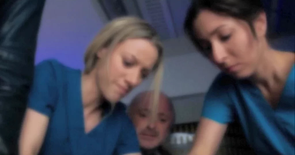 Bo's blurry view of Lauren (Zoie Palmer) and Lisa (Nadine Djoury) working on her wound while Trick (Rick Howland) looks on.k - Lost Girl 503